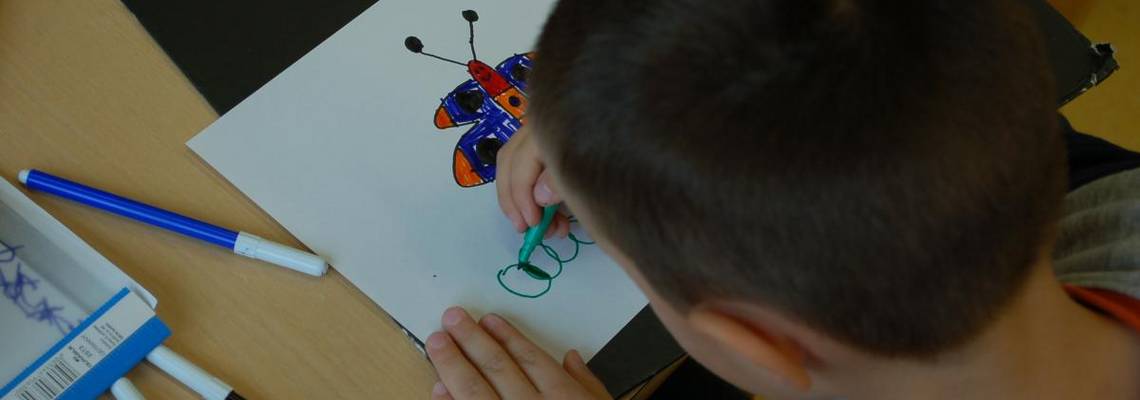 Ein Junge malt einen Schmetterling auf ein weißes Blatt.