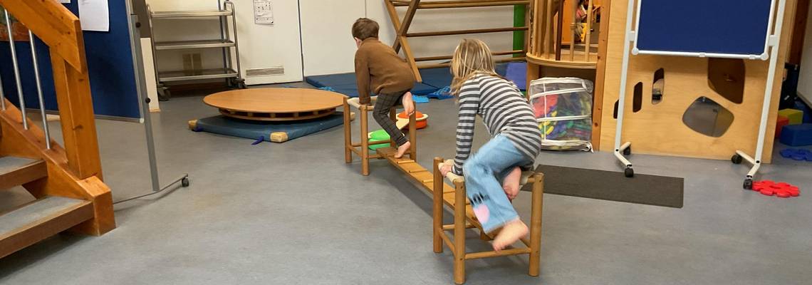 Zwei Kinder balancieren und klettern auf einer aufgebauten Bewegungslandschaft aus Holzmaterialien