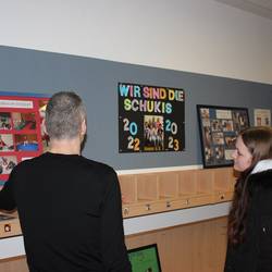 Der Kita- Leiter zeigt auf Informationswänden einer Schülerin die Schwerpunkte der Kita.