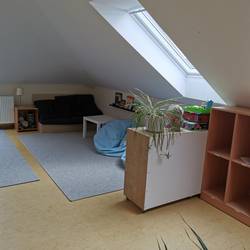 Ein Raum unter der Dachschräge ist zu sehen. Im vorderen Bereich steht ein Regal für die Schulranzen der Kinder. Im hinteren Bereich ist eine Sofaecke zu sehen.