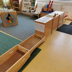 Gruppenraum Blick in den Gruppenraum der Krippe. Verschiedene Bewegungselemente sind zu sehen, sowie eine kleine Spielküche und ein Motorikwürfel.