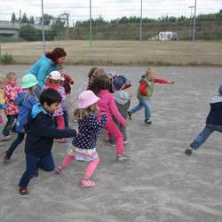 Kinder führen Bewegungsspiele auf dem Bolzplatz durch.