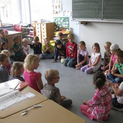Kinder sitzen gemeinsam mit Lehrerin im Sitzkreis.