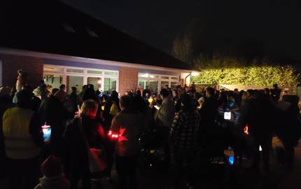 Eine Gruppe von Menschen mit Laternen stehen vor einem hell erleuchteten Gebäude.