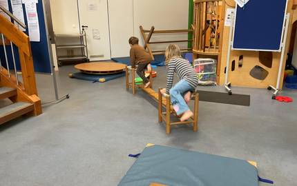 Zwei Kinder balancieren und klettern auf einer aufgebauten Bewegungslandschaft aus Holzmaterialien